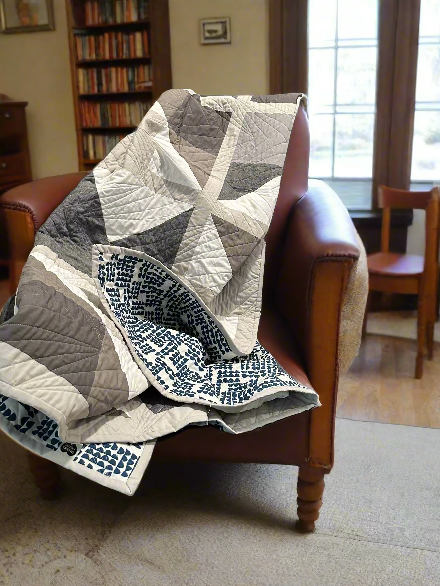 Quilt draped over a brown leather chair in a room with bookshelves and a window.